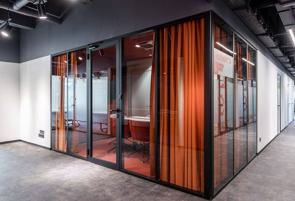 Black-framed glass office room with orange curtains inside.