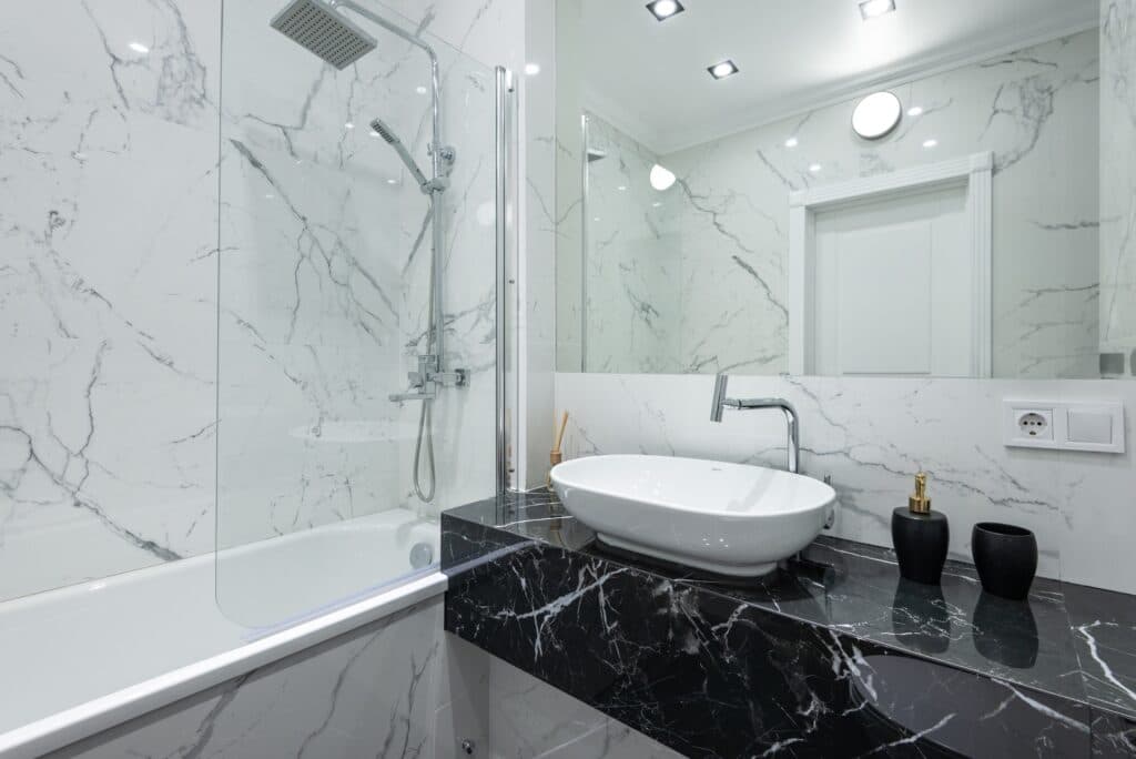 Marble bathroom with a glass shower screen beside a bathtub.