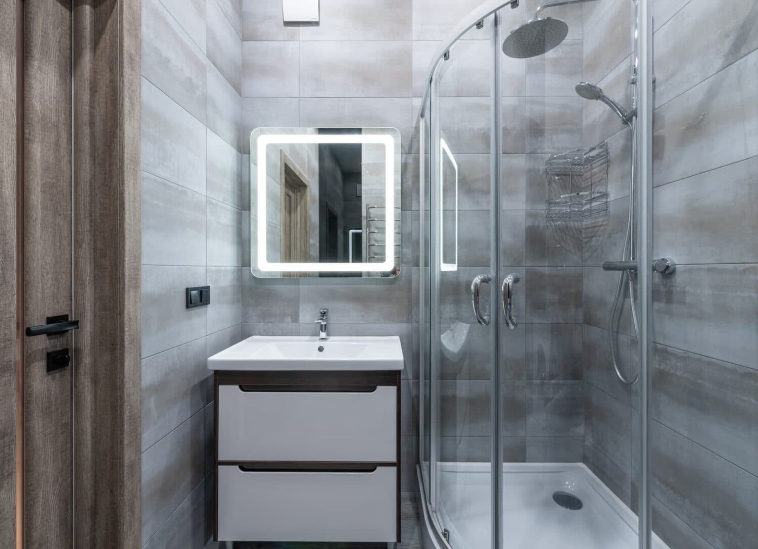 Grey tiled bathroom with a curved glass shower enclosure.