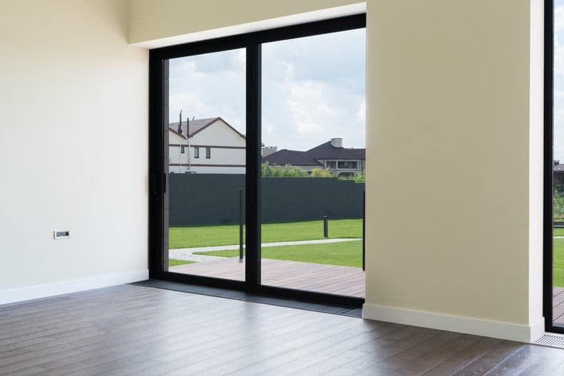 Black-framed sliding glass patio door beside an unfurnished room, looking onto a deck and lawn.