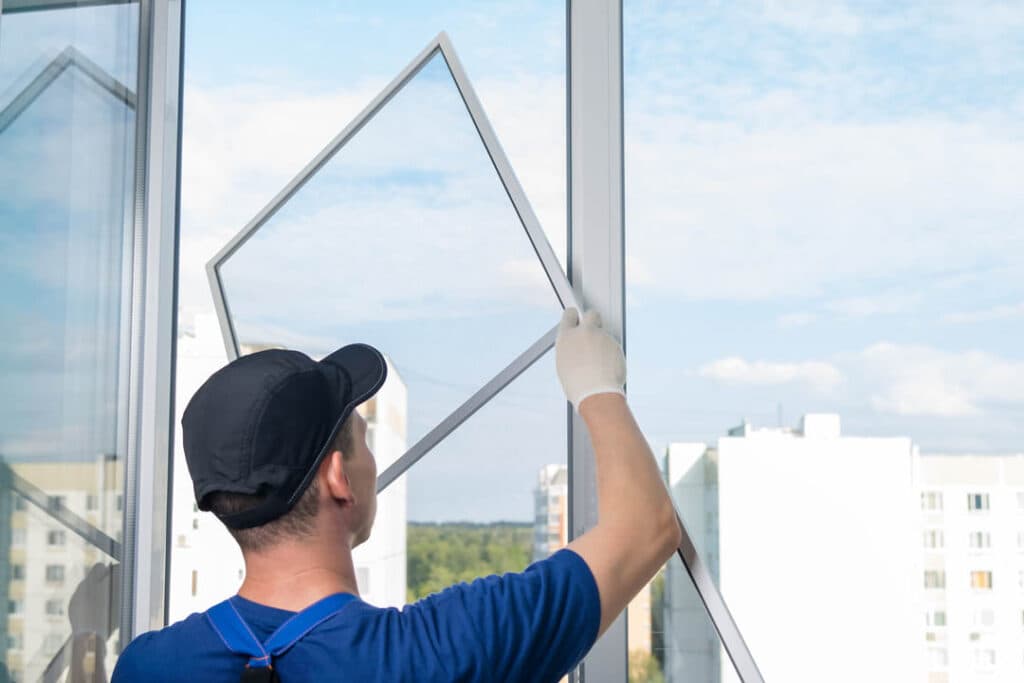 Worker holding a rectangular framed panel beside a white window.