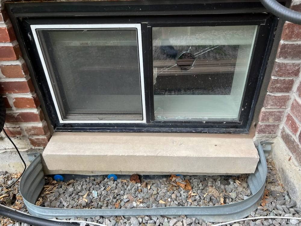 Basement window in a brick wall with a hole and cracks in one pane.
