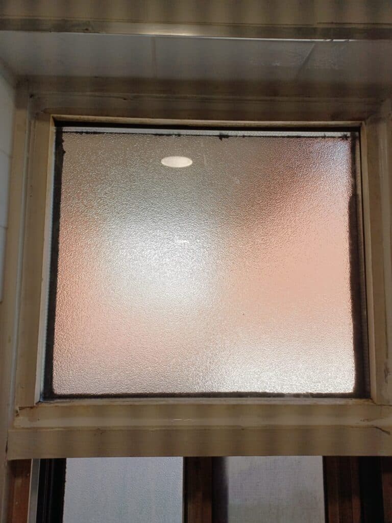 Textured translucent glass in a painted window frame, with blurred light visible behind the pane.