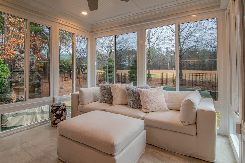 Sunroom with tall windows on two sides and a white sectional sofa facing the garden.