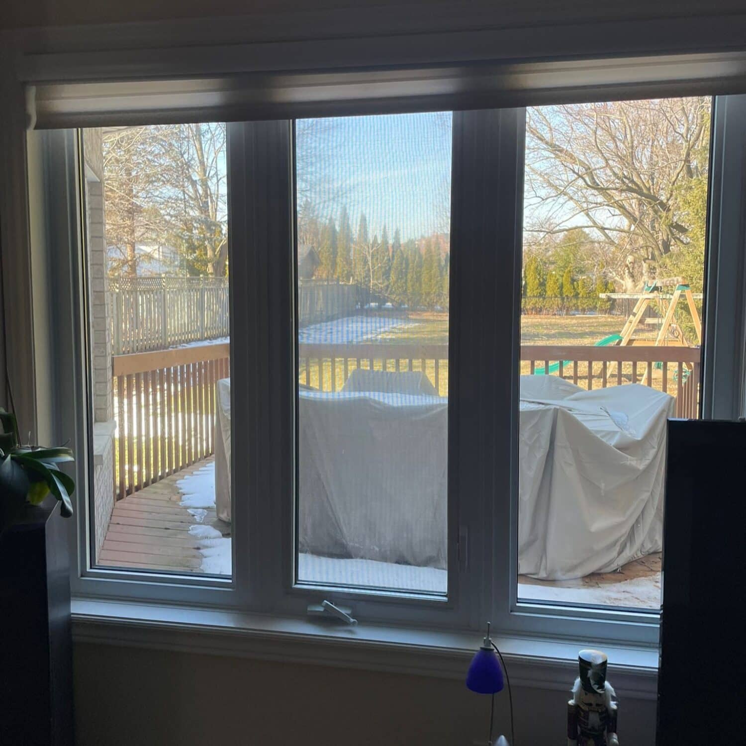 Residential window overlooking a snowy deck with covered furniture.