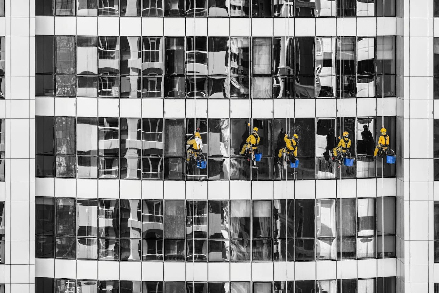 Window cleaners in yellow gear suspended beside a reflective glass facade.